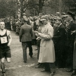Czarno biała fotografia przedstawiająca widownię oraz biegnącego sportowca.