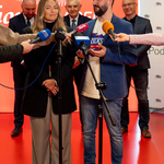 Dwoje organizatorów stoi przed mikrofonami podczs konferencji.