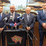 Marszałek Łukasz Prokorym mówi do mikrofonu przy mównicy, obok stoją inni przedstawiciele miasta.