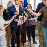 Przedstawiciel organizacji „Caritas” stoi przed mikrofonami.