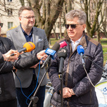 Mężczyzna udziela wywiadu stojąc przed mikrofonami, obok stoi zastępca prezydenta Rafał Rudnicki oraz dziennikarz.