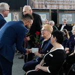 Radny wręcza kobiecie różę, wokół siedzą i stoją inni uczestnicy wydarzenia.