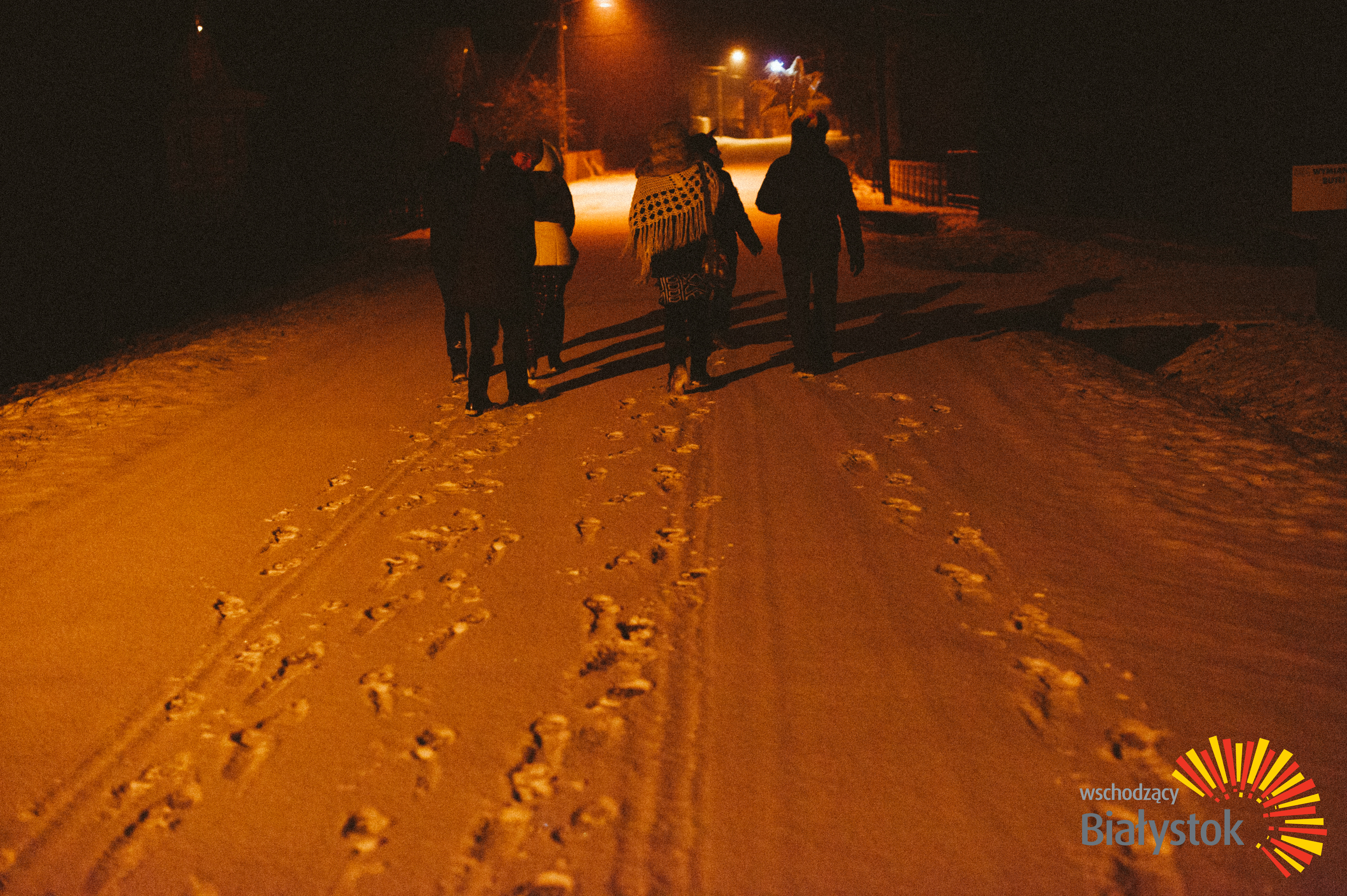 Osoby idące wieczorową porą po zaśnieżonej drodze