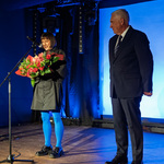 Prezydent Tadeusz Truskolaski stoi na scenie obok kobiety która trzyma bukiet kwiatów i mówi do mikrofonu.