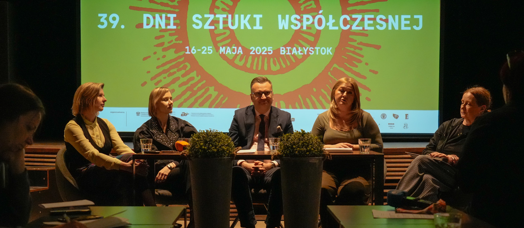 Uczestnicy konferencji siedzą przy stole, w tle wyświetlana grafika z tekstem „39. DNI DNI SZTUKI WSPÓŁCZESNEJ 16-25 MAJA 2025 BIAŁYSTOK”.
