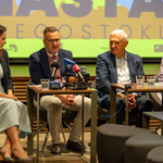 Zastępca prezydenta Rafał Rudnicki mówi do mikrofonów które leżą na stoliku, obok siedzą inni przedstawiciele Miasta.