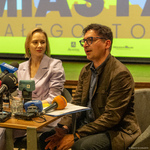Mężczyzna mówi do mikrofonów podczas konferencji prasowej, obok siedzi kobieta.