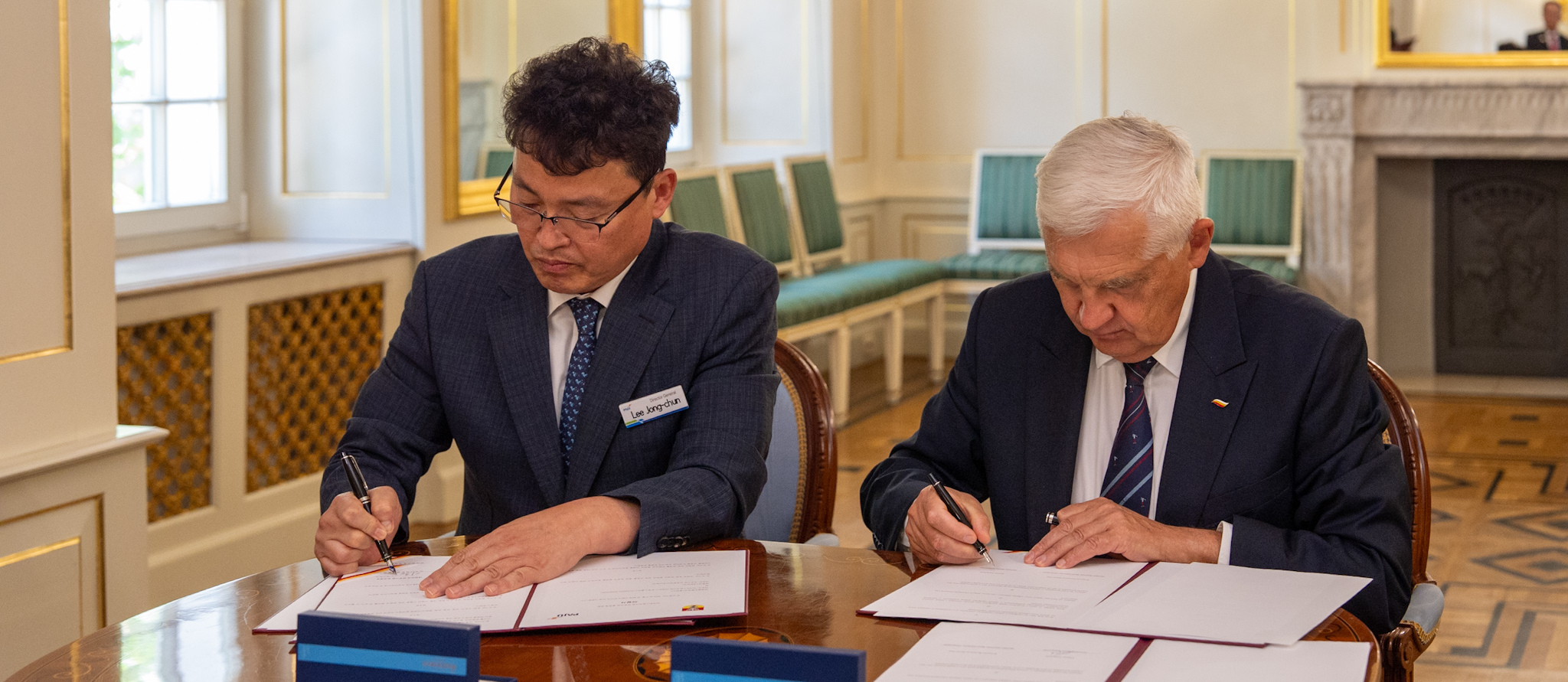 Prezydent Tadeusz Truskolaski oraz mężczyzna podpisują dokumenty przy stole.