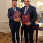 Prezydent Tadeusz Truskolaski podaje dłoń mężczyźnie, oboje trzymają w rękach teczki z dokumentami.