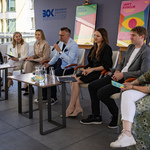 Kilkoro uczestników konferencji prasowej siedzi na krzesłach, wśród nich zastępca prezydenta Rafał Rudnicki mówi do mikrofonu.