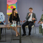 Uczestnicy konferencji siedzą na krzesłach, mężczyzna mówi do mikrofonu.
