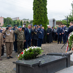 Mundurowi oraz kilku innych uczestników uroczystości salutuje stojąc w kilku rzędach.