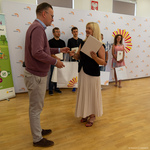 Zastępca prezydenta Rafał Rudnicki wręcza kobiecie list gratulacyjny oraz upominek, w tle stoją inni zwycięzcy.