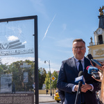 Zastępca prezydenta Rafał Rudnicki mówi do mikrofonów, obok stoi dziennikarka, po drugiej stronie rama z obrazem na szkle.