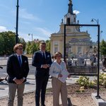 Trzy osoby stoją obok ramy z obrazem i opisem na szkle.