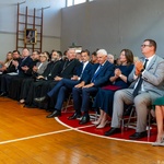 Przedstawiciele Miasta i instytucji, goście i uczniowie siedzą na krzesłach podczas uroczystości na sali gimnastycznej.
