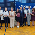 Grupa uczniów i nauczycieli stoi trzymając medale i listy gratulacyjne.