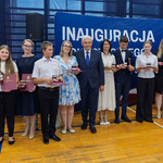 Grupa uczniów i nauczycieli stoi trzymając medale i listy gratulacyjne podczas uroczystości.