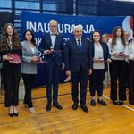 Kilkunastu uczniów i nauczycieli stoi trzymając medale i listy gratulacyjne.