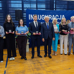 Grupa uczniów i nauczycieli stoi trzymając medale i listy gratulacyjne.