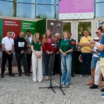 Studentka udziela wywiadu podczas konferencji prasowej, w tle stoją inni uczestnicy oraz dziennikarze.