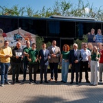 Kilkunastu uczestników spotkania stoi obok zaparkowanego autobusu.