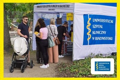 Przy namiocie w parku stoi kilka osób, w dole zdjęcia logo Uniwersyteckiego Szpitala Klinicznego w Białymstoku.