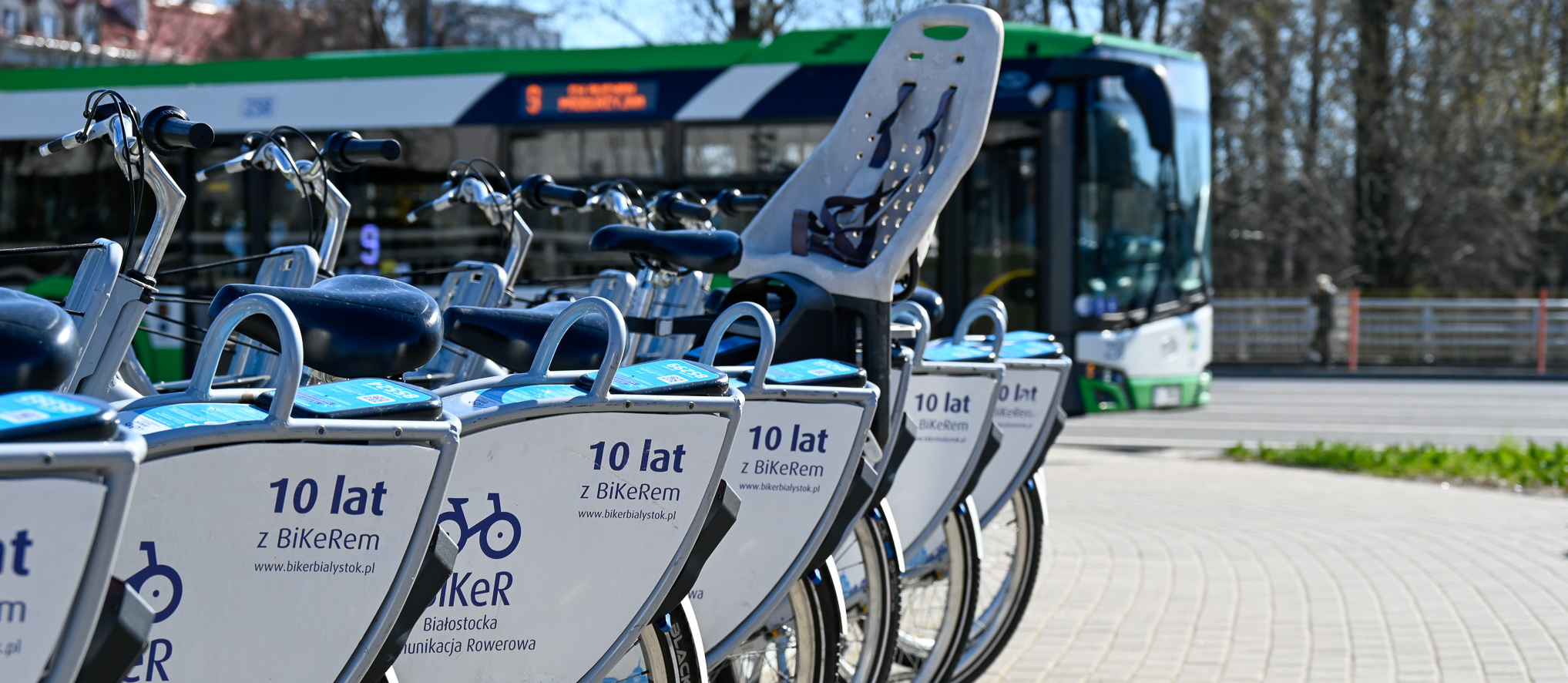 Rowery BiKeR stoją przy stacji, w tle jedzie autobus BKM.