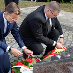 Zastępca prezydenta Tomasz Klim oraz wojewoda Jacek Brzozowski poprawiają wstęgi przy złożonych wieńcach.