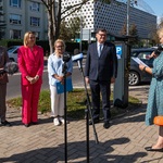 Uczestnicy konferencji stoją przy parkomacie przed mikrofonami.