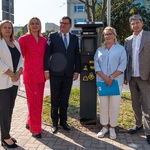 Kilku uczestników biorących udział w konferencji prasowej stoi obok nowego parkomatu.