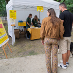 Dwie osoby z psem stoją obok stoiska z żółtymi plakatami.
