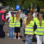 Uczniowie w kamizelkach odblaskowych wręczają elementy odblaskowe przechodniom
