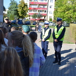 Dzieci stoją przed szkołą i rozmawiają z dwoma policjantkami