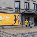 Dwie kobiety idą obok budynku Białostockiego Ośrodka Kultury, na którym umieszczony jest plakat promujący festiwal Ciekawi Świata.
