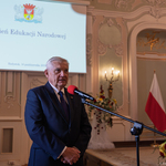 Prezydent Tadeusz Truskolaski mówi do mikrofonu, w tle wyświetlana grafika z tekstem „Dzień Edukacji Narodowej”.