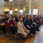 Uczestnicy zgromadzeni w Auli Magna siedzą na krzesłach podczas wydarzenia.