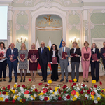 Wyróżnione osoby stoją z listami gratulacyjnymi w rękach podczas wydarzenia.