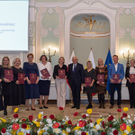 Wyróżnione osoby stoją z listami gratulacyjnymi w rękach podczas wydarzenia.