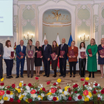 Grupa wyróżnionych osób stoi z listami gratulacyjnymi w rękach podczas wydarzenia.