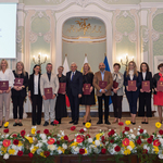 Grupa wyróżnionych osób stoi z listami gratulacyjnymi w rękach podczas uroczystości.