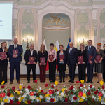 Grupa wyróżnionych osób stoi z teczkami obok prezydenta Tadeusza Truskolaskiego.