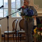 Podlaska kurator Agnieszka Krokos-Jaczyło mówi do mikrofonu i trzyma kwiaty.