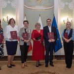 Siedem osób z listami gratulacyjnymi w rękach stoi obok siebie.