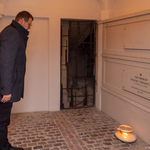 Zastępca prezydenta Tomasz Klim pochyla głowę przy grobie Arcybiskupa Edwarda Ozorowskiego pochowanego w krypcie bazyliki białostockiej, Pod pamiątkową tablicą stoi zapalony znicz 