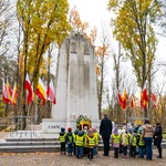 Dzieci w odblaskowych kamizelkach stoją przed pomnikiem 