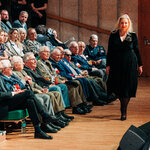 Monika Szarejko - kierowniczka Działu Wystawy Stałej w Muzeum Pamięci Sybiru ubrana w czarną sukienkę podąża w stronę sceny. Na auli siedzą ludzie 