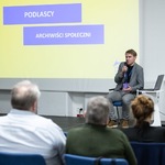 Mężczyzna mówi do mikrofonu siedząc na scenie, w tle wyświetlana grafika z tekstem „Podlascy Aktywiści Społeczni”.