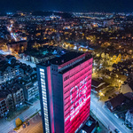 Podświetlony na czerwono budynek Urzędu Miejskiego, w tle miasto nocą.