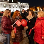 Cztery kobiety rozmawiają, trzymają w rękach czerwone chorągiewki i balony.